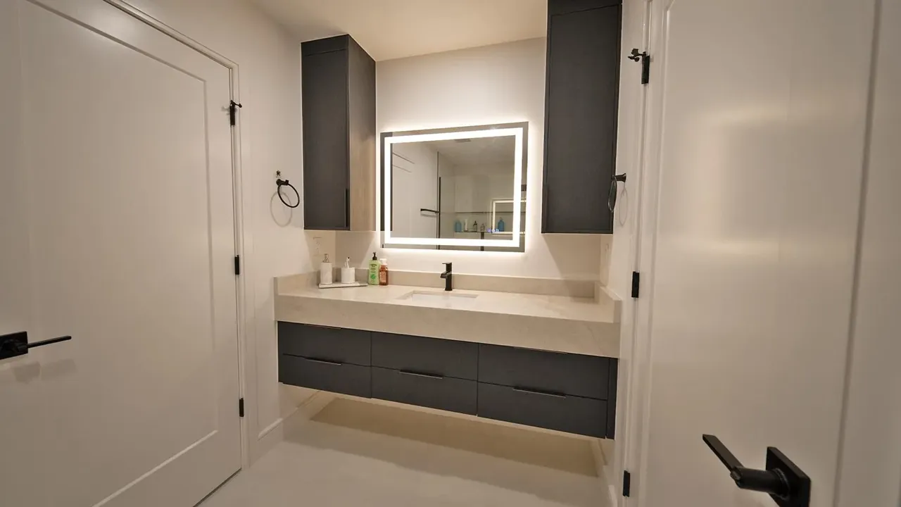 Black floating vanity with a lit mirror and wall cabinets on each side by Mason Oak Carpentry in Detroit, MI