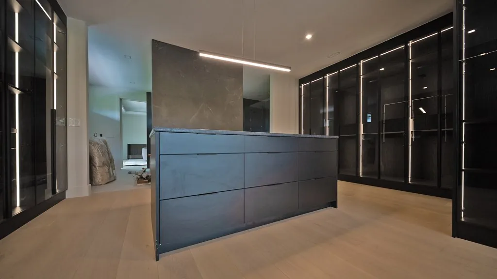 Walk-in closet with black glass-front wardrobes, LED strip lighting and a drawer island by Mason Oak Carpentry in Detroit, MI