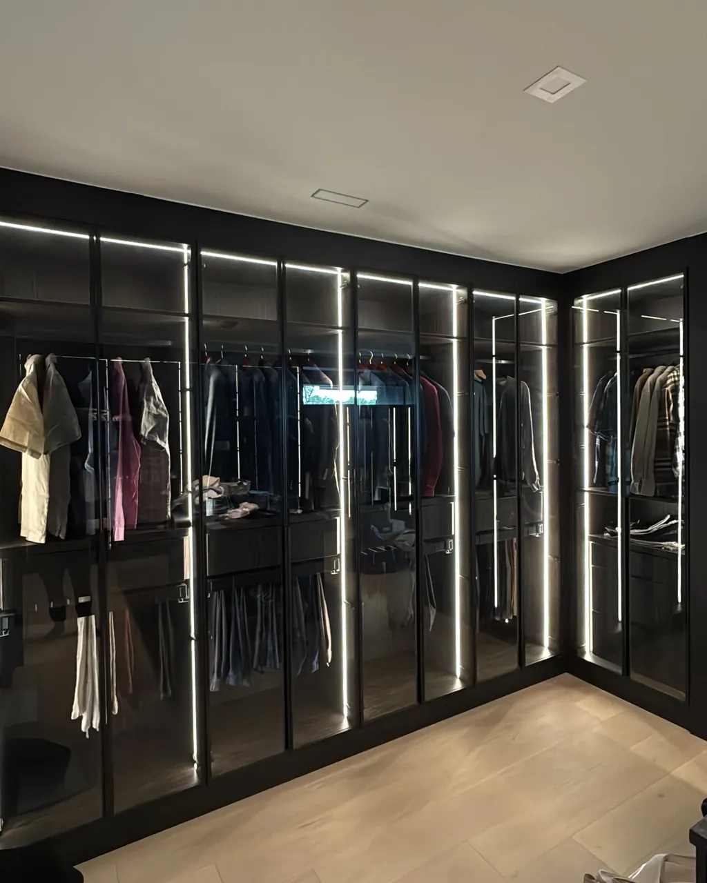 Walk-in closet with floor-to-ceiling glass wardrobe doors and built-in lighting by Mason Oak Carpentry in Detroit, MI