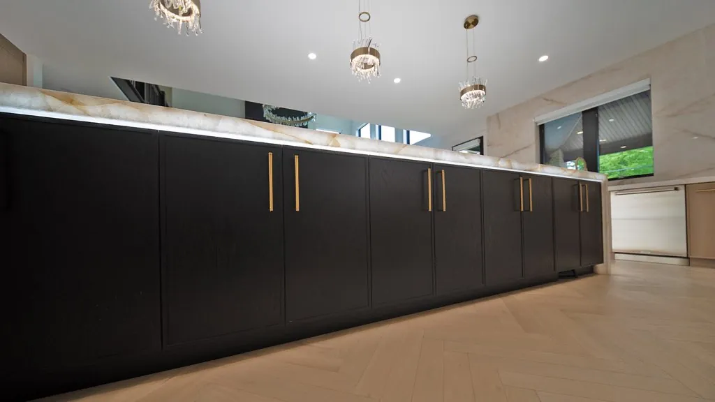 Black island cabinets with brass pulls under a backlit stone countertop by Mason Oak Carpentry in Detroit, MI