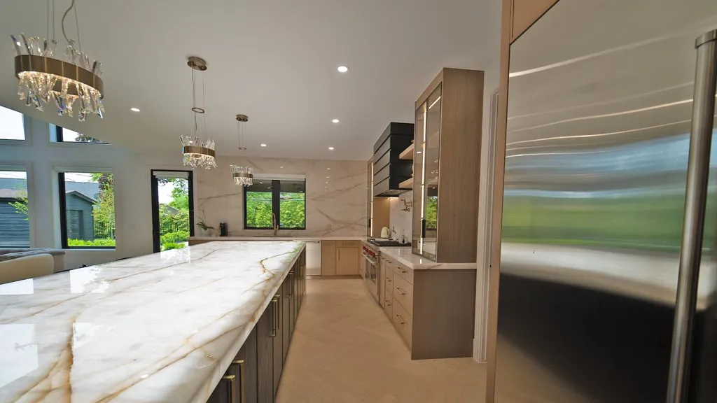 Long kitchen island with dark base cabinets and a light wood kitchen beyond by Mason Oak Carpentry in Detroit, MI