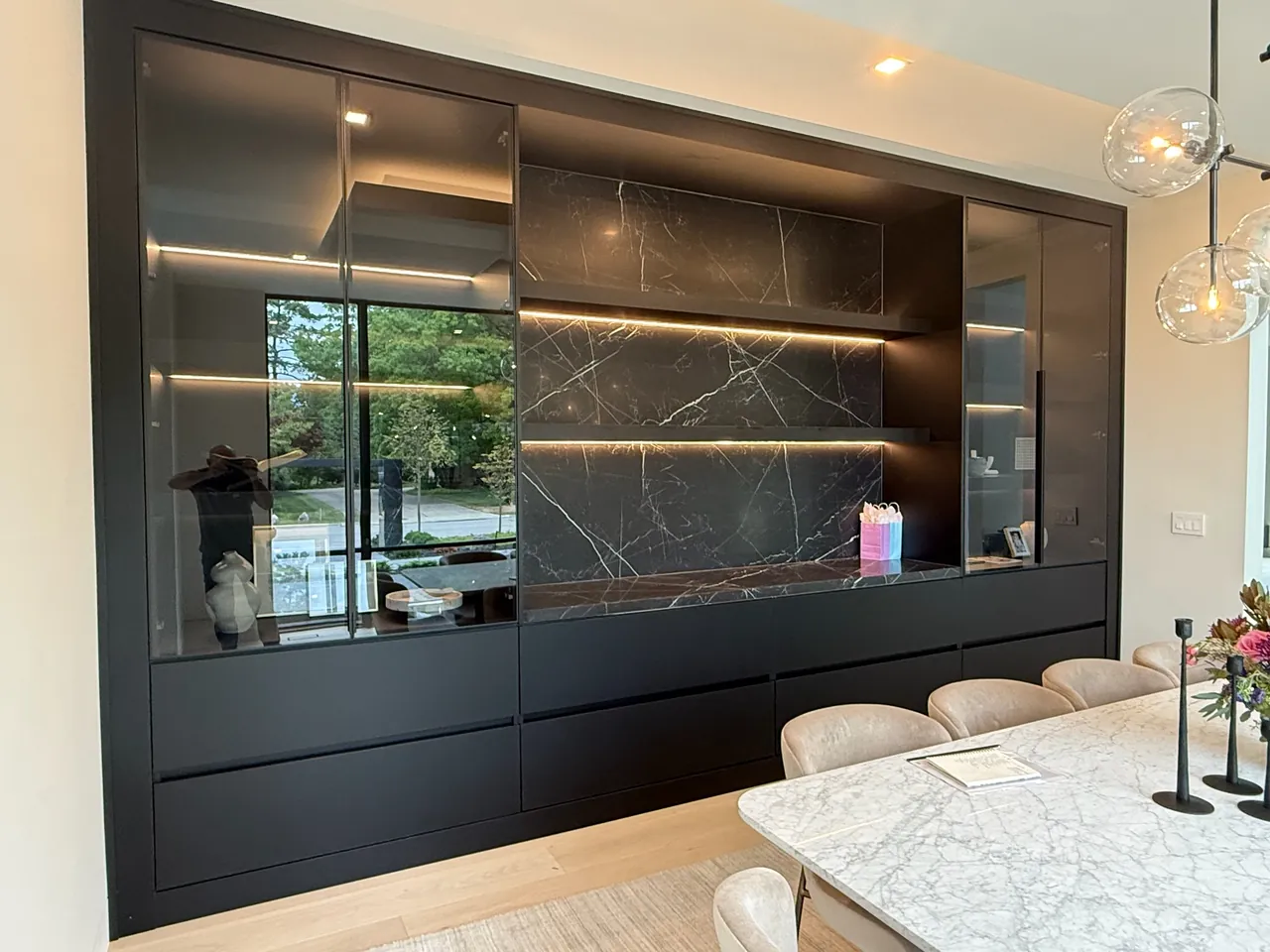 Black built-in bar wall with lit glass cabinets and a stone backsplash by Mason Oak Carpentry in Detroit, MI