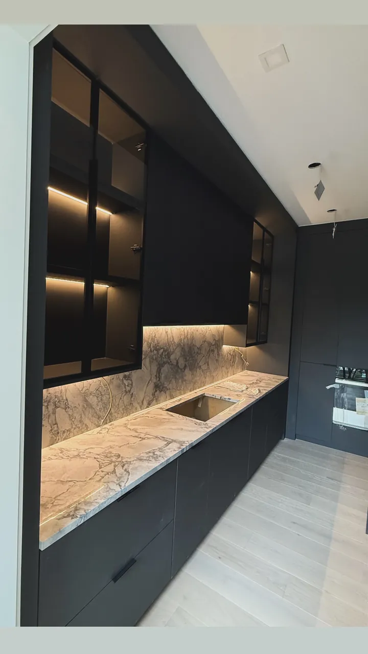 Black galley kitchen with lit glass upper cabinets and a stone countertop by Mason Oak Carpentry in Detroit, MI