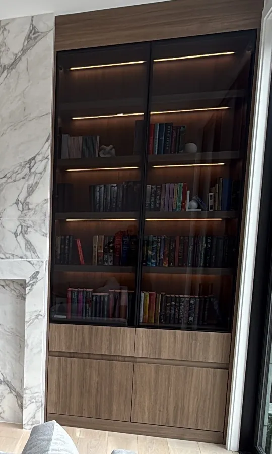 Lit glass-front bookcase with walnut base cabinets beside a stone fireplace wall by Mason Oak Carpentry in Detroit, MI