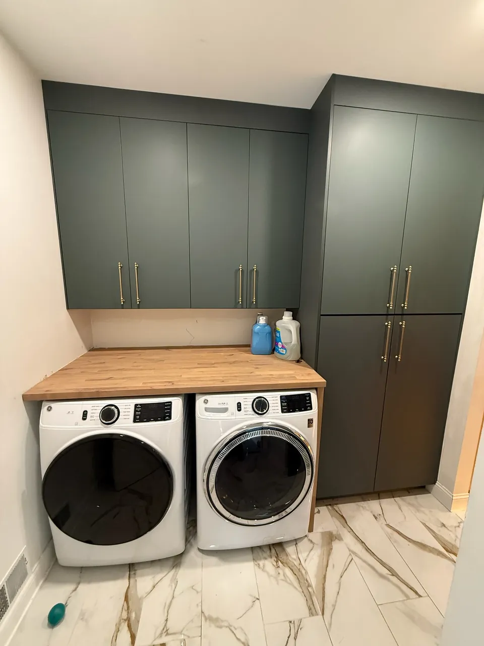 Laundry room with green cabinets and a wood countertop over the washer and dryer by Mason Oak Carpentry in Detroit, MI