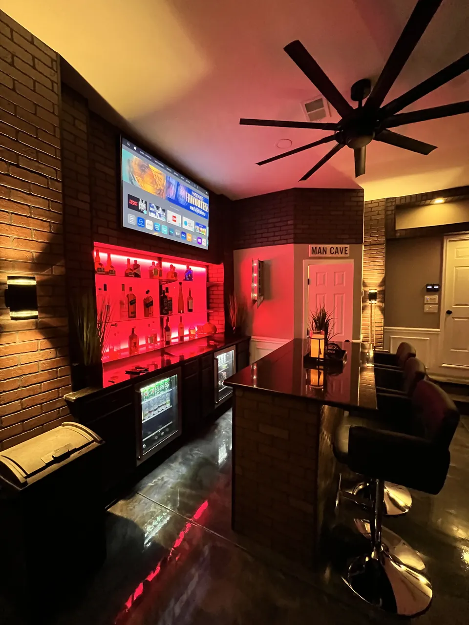 Garage back bar with red-lit glass shelving, a brick surround and a black bar top by Mason Oak Carpentry in Detroit, MI