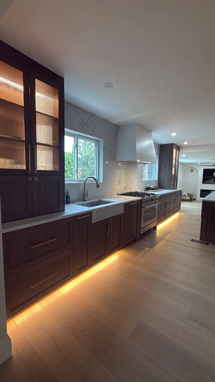 Dark wood kitchen with glass upper cabinets and lighting under the base cabinets by Mason Oak Carpentry in Detroit, MI