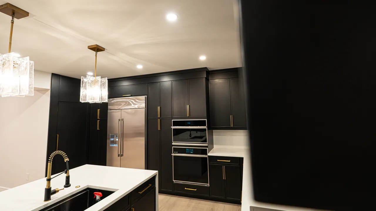 Black kitchen with built-in ovens, a tall fridge wall and a white island by Mason Oak Carpentry in Detroit, MI