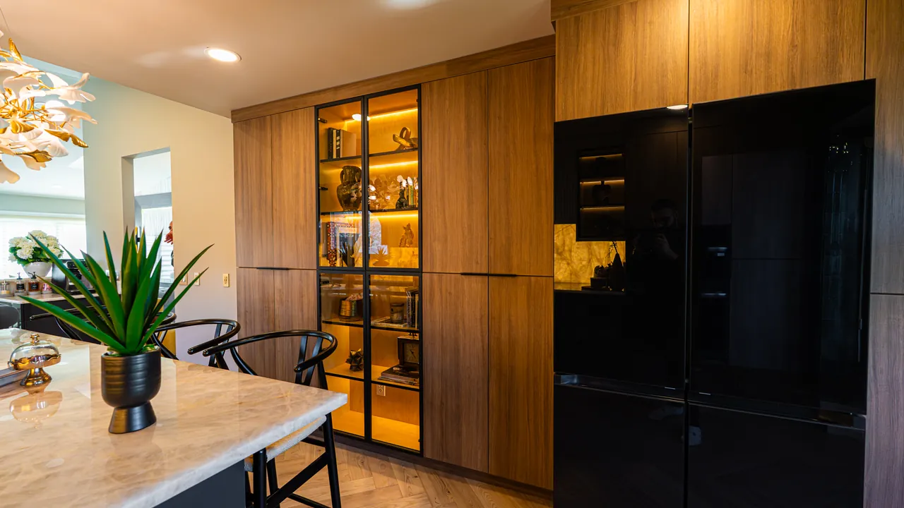 Walnut tall cabinets with a lit glass display cabinet beside a black fridge by Mason Oak Carpentry in Detroit, MI