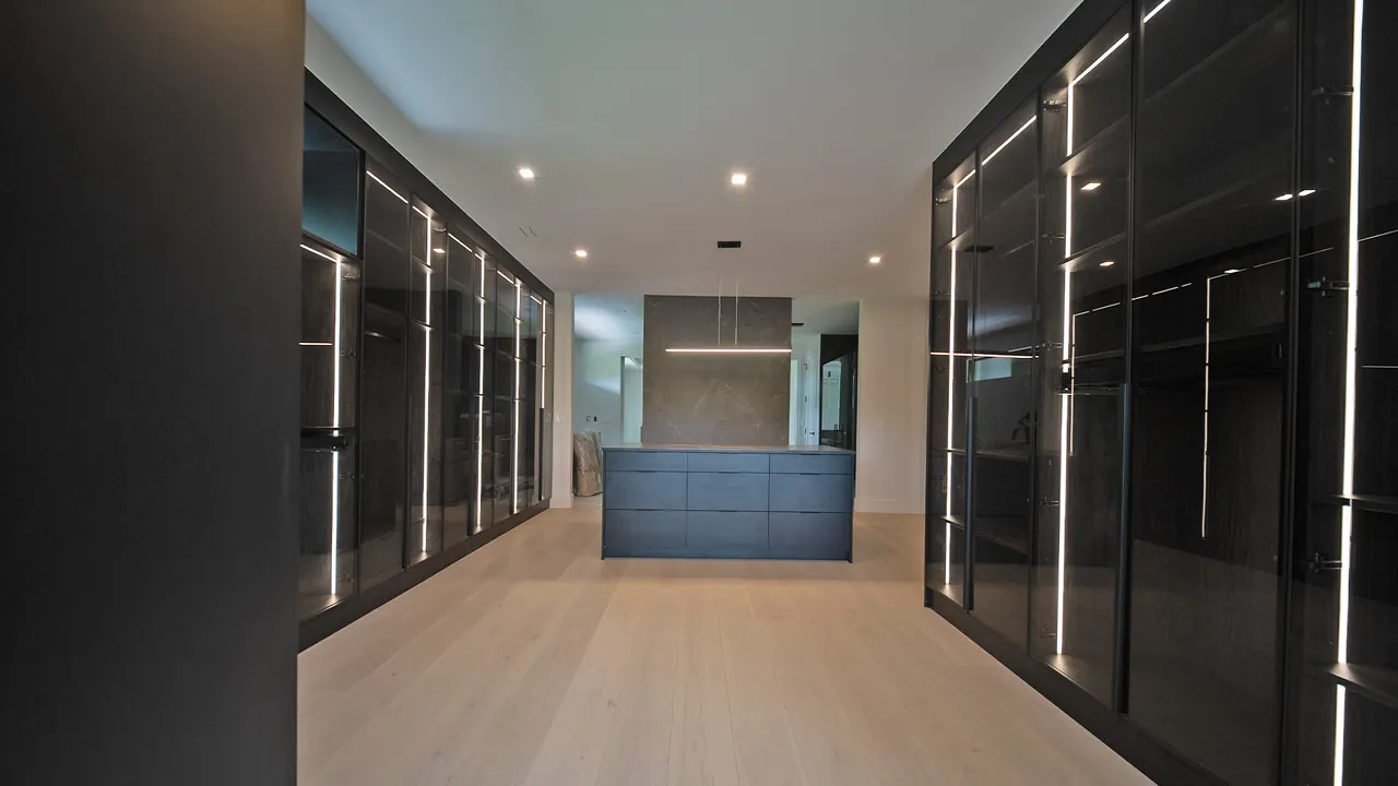 Walk-in closet with lit black glass wardrobes on both sides by Mason Oak Carpentry in Detroit, MI