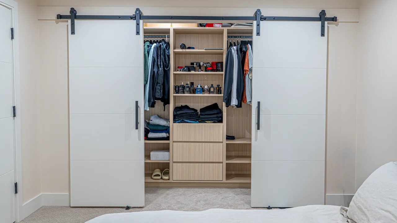 Reach-in closet with white barn doors and light wood drawers by Mason Oak Carpentry in Detroit, MI