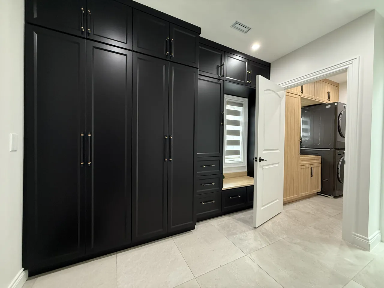 Black mudroom wall with tall cabinets, a bench nook and a laundry room beyond by Mason Oak Carpentry in Detroit, MI