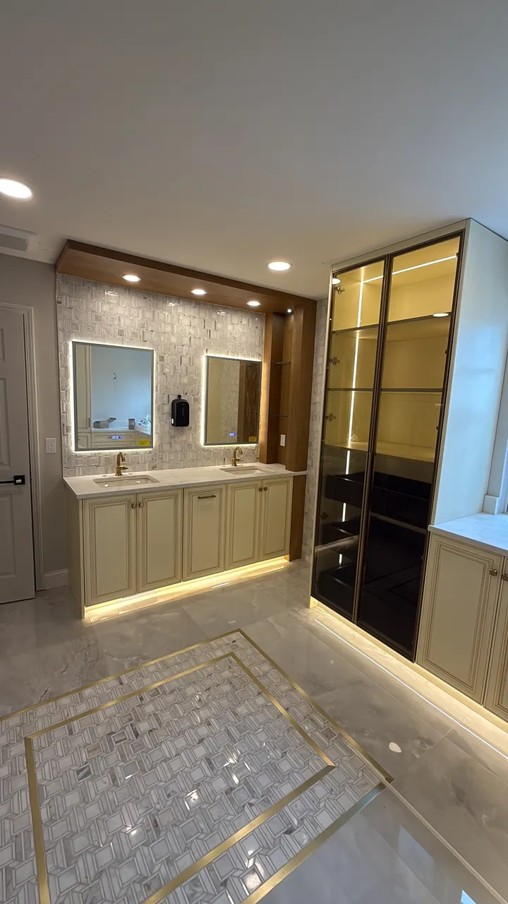 Cream double vanity with lit mirrors and a glass display cabinet by Mason Oak Carpentry in Detroit, MI
