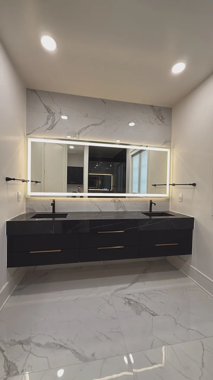 Floating black double vanity under a lit mirror in a marble bathroom by Mason Oak Carpentry in Detroit, MI