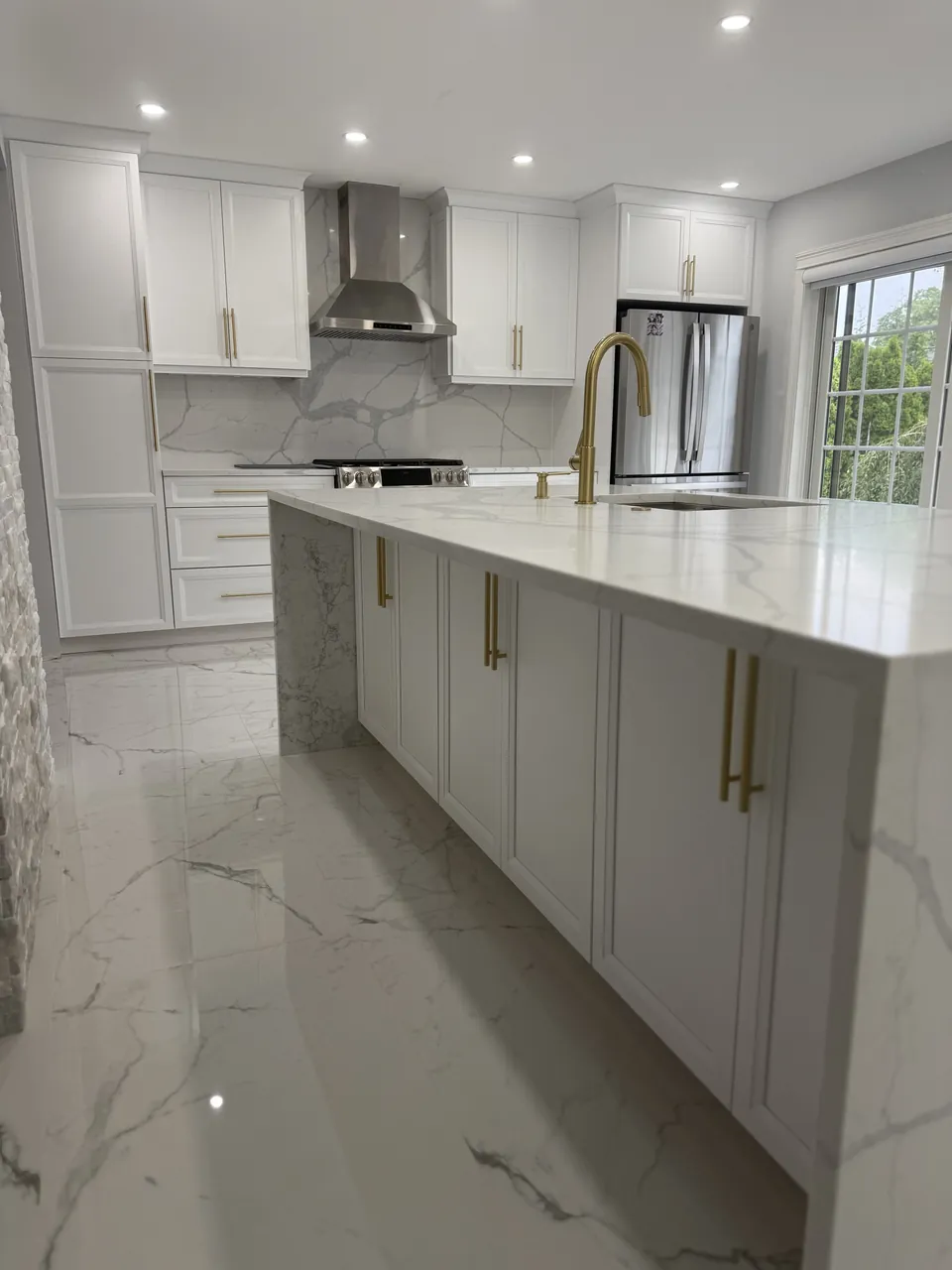 White kitchen with a waterfall marble island, brass hardware and a stainless hood by Mason Oak Carpentry in Detroit, MI